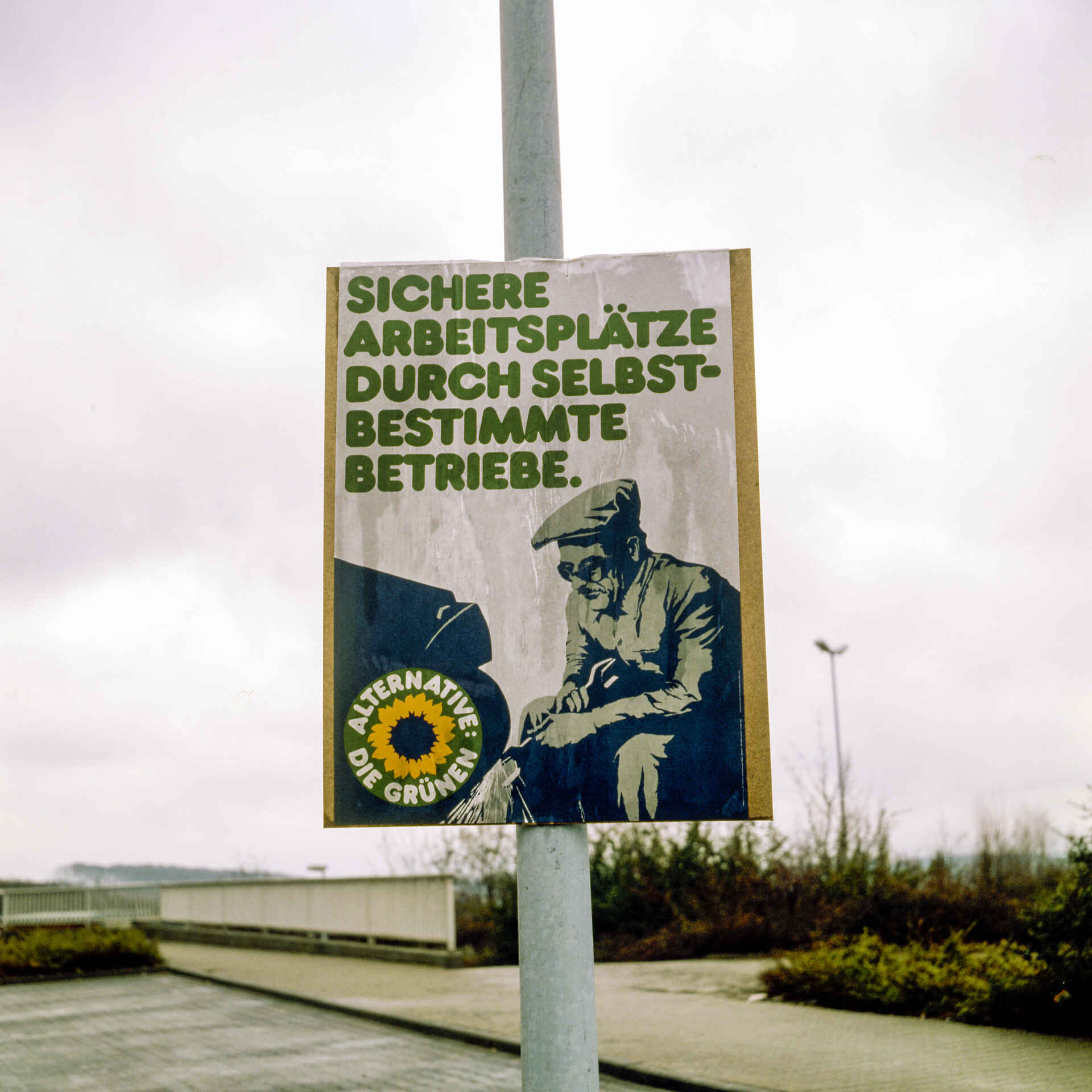 Damals haben sich die Grünen noch was getraut – und 8 % bekommen. (Foto: Martin Frech, 3/1984) Farbbild (Digitalisat vom Mittelformatdia): Wahlplakat der Partei ›Die Grünen‹ zur Landtagswahl 1984 in Baden-Württemberg. Der Slogan lautet: ›Sichere Arbeitsplätze durch selbstbestimmte Betriebe‹. (Foto: Martin Frech, 3/1984)