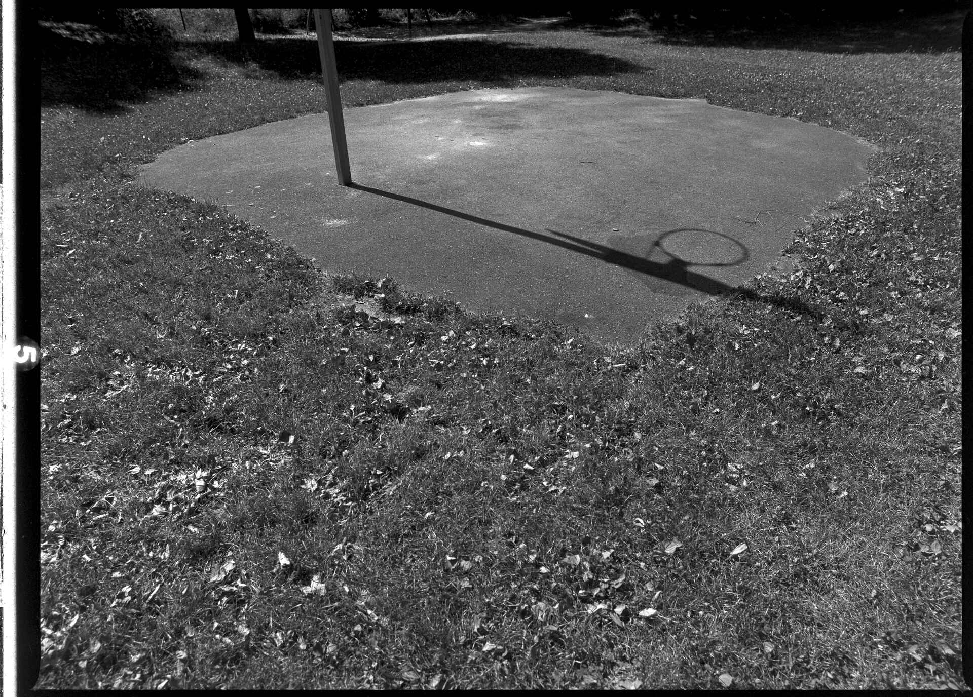 knapp 40°C im Schatten Schwarzweißbild (digitalisiert vom Fomapan-100-Rollfilmnegativ): Schatten eines Basketballkorbs auf einem Spielplatz in Kirchentellinsfurt/Tübingen.