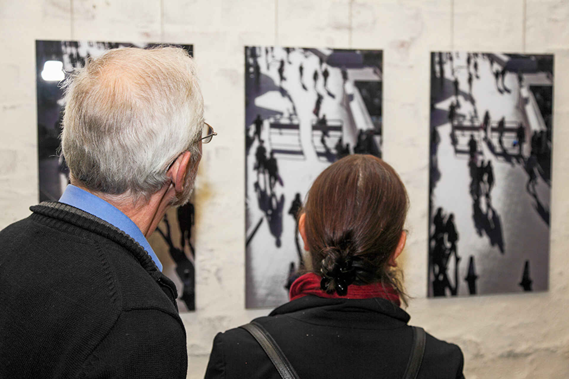 Impression von der Vernissage in der schaelpic photokunstbar, Köln (Foto: Theo Hilgers, 11/2012) Farbbild: Zwei Personen schauen sich Fotos an, die an der Wand der schaelpic photokunstbar (Köln) hängen. (Foto: Theo Hilgers, 11/2012)