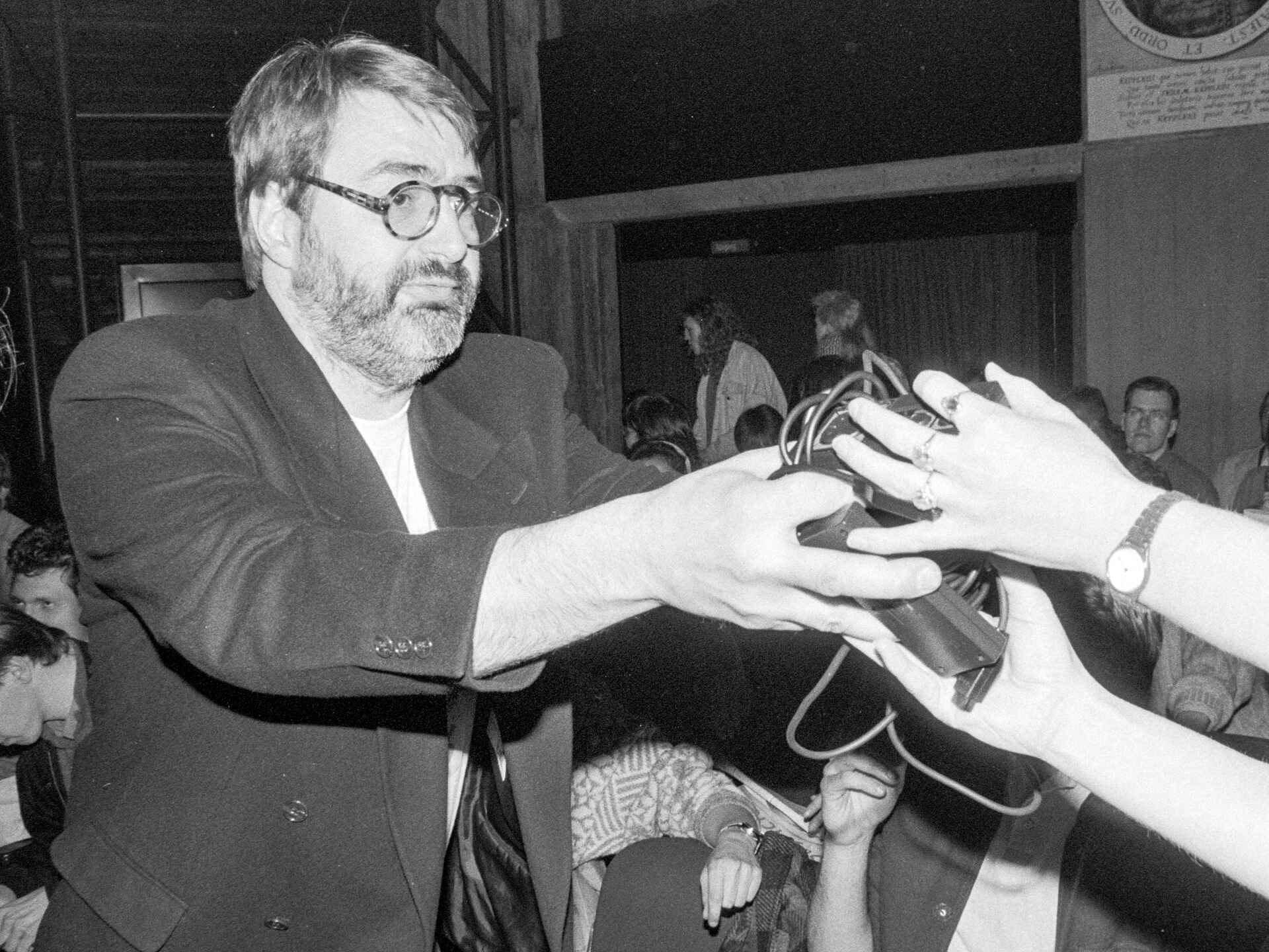 Schwarzweißbild: Der Filmemacher Peter Krieg (Wilhelm Gladitz) verteilt vor einer interaktiven Kinovorführung (ELVIS) seines Film ›Suspicious Minds‹ kabelgebundene Gamecontroller im Kino. (Foto: Martin Frech, 3/1991)