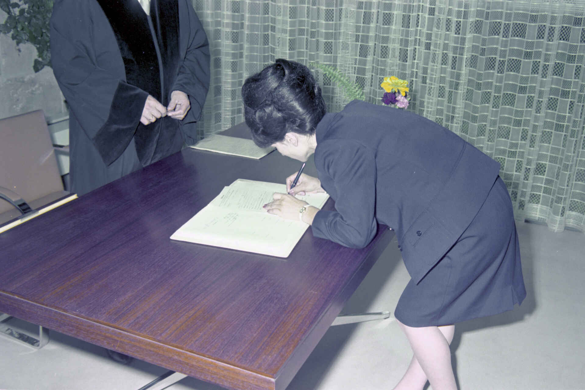 Szene auf dem Standesamt der Stadt Reutlingen (Foto: StadtA Rt./Dohm, 1967) Farbbild: Eine Frau unterschreibt eine Urkunde im Beisein einer Amtsperson. (Foto: StadtA Rt./Dohm, 1967)