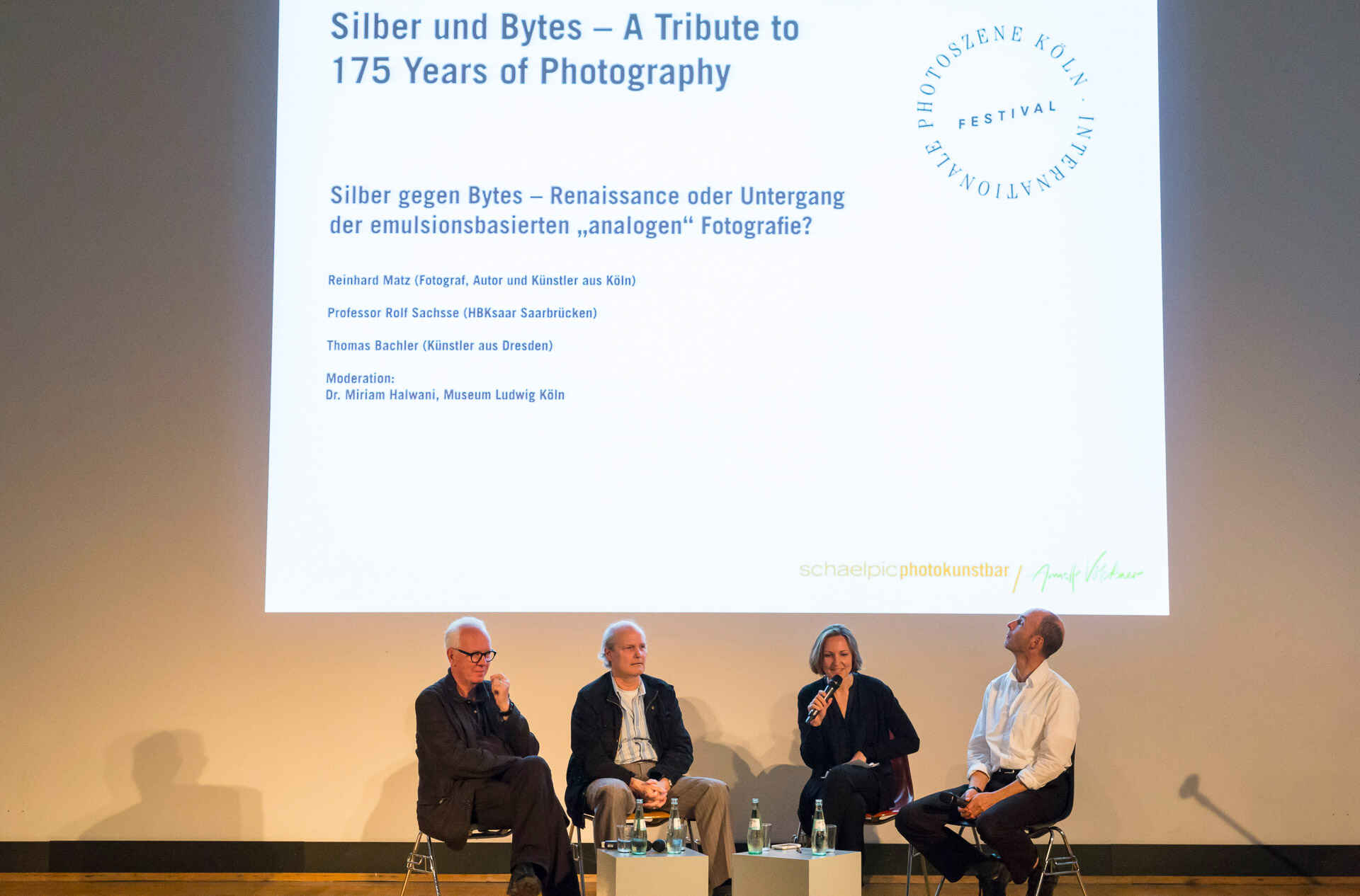 Silber und Bytes | Silber gegen Bytes; Podiumsdiskussion: Rolf Sachsse (HBKsaar Saarbrücken), Reinhard Matz (Fotograf, Autor und Künstler aus Köln), Miriam Halwani (Museum Ludwig), Thomas Bachler (Künstler aus Dresden) (v.li.). (Foto: Markus Bollen, 9/2014) Auf einem Podium sitzen vier Personen: Rolf Sachsse (HBKsaar Saarbrücken), Reinhard Matz (Fotograf, Autor und Künstler aus Köln), Miriam Halwani (Museum Ludwig), Thomas Bachler (Künstler aus Dresden) (v.li.). An die Wand hinter ihnen ist projiziert ›Silber und Bytes – 175 Years of Photography‹. (Foto: Markus Bollen, 9/2014)