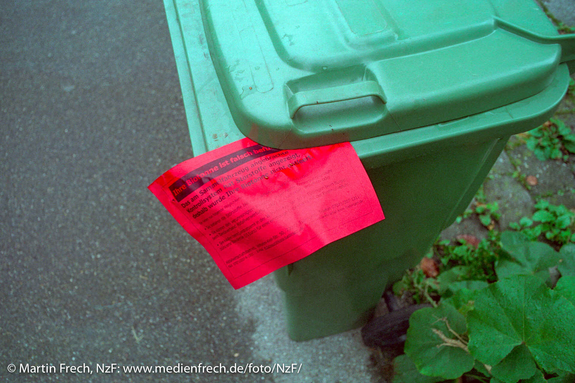 Farbbild: Grüne Tonne für Bioabfall im Anschnitt von oben. Unter dem Deckel klemmt ein Zettel mit dem Hinweis auf unzulässigen Inhalt. (Foto: Martin Frech, 10/2017)