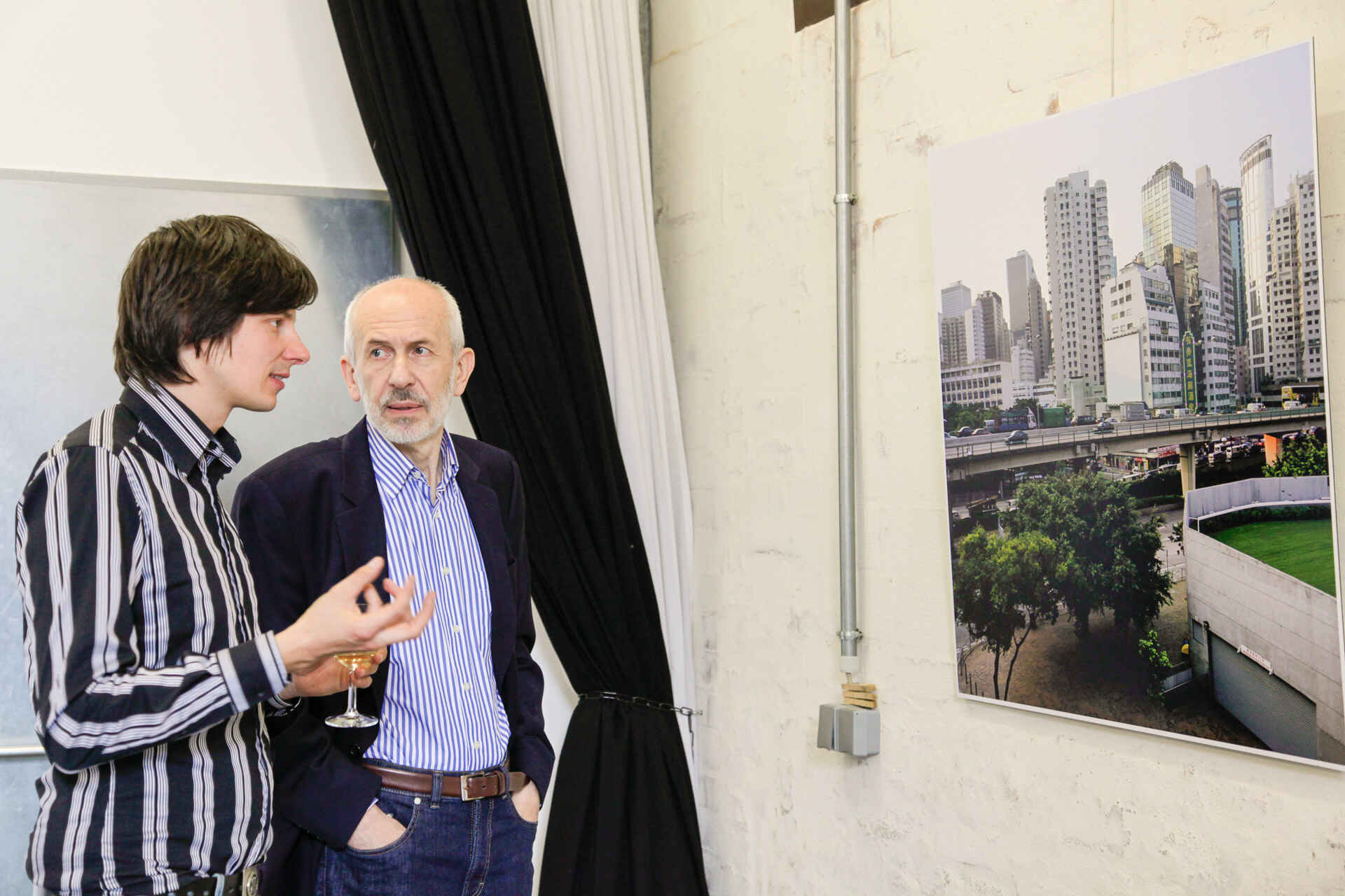 Farbbild: Zwei Männer im Gespräch (links der Fotograf Tobias Vollmer, rechts ein Besucher der Ausstellung), an der Wand hängt eine großformatige Stadtansicht (Foto: Andrea Otto, 6/2012)