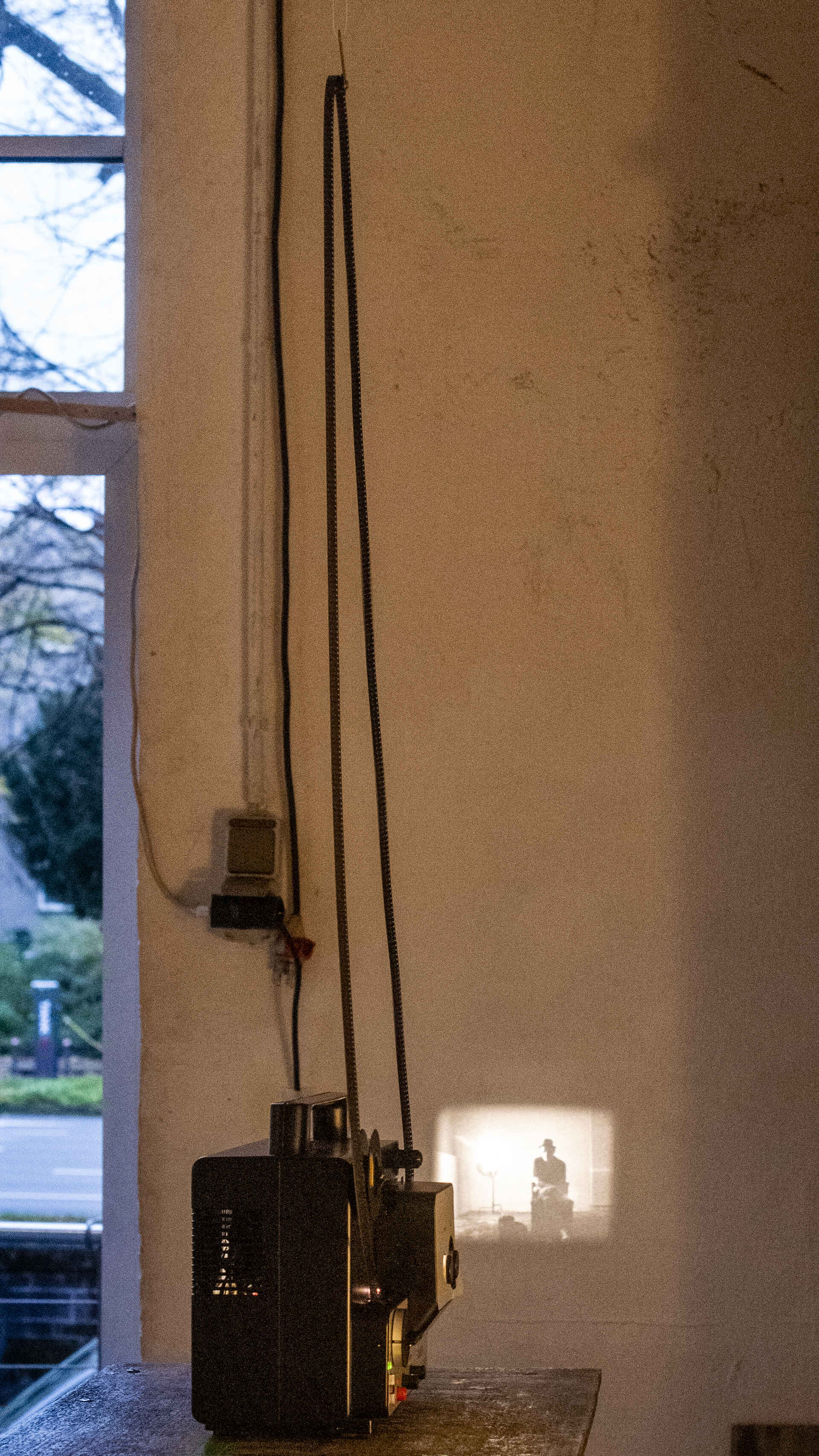 Farbfoto: Super-8-Projektor, der einen Loop abspielt, mit projiziertem Bild im Hintergrund. (Foto: Martin Frech, 11/2025)