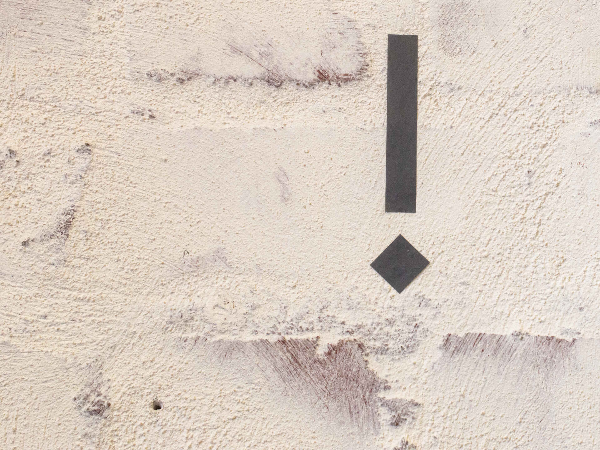 Farbbild (born digital): Dunkelgraues Ausrufezeichen aus Teilen von Folienlettern, angebracht an verputzter Ziegelwand, schaelpic photokunstbar Köln-Mühlheim.