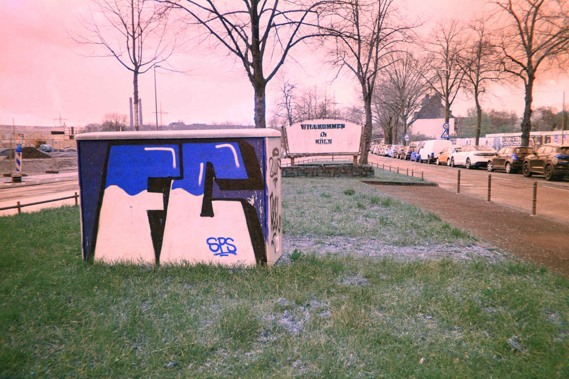 Gruß, Köln (Foto: Martin Frech, 3/2026) Farbbild (invertiertes Digitalisat des Falschfarben-Colornegativs): Grünanlage in Köln mit einem Willkommensgruß (Foto: Martin Frech, 3/2026)