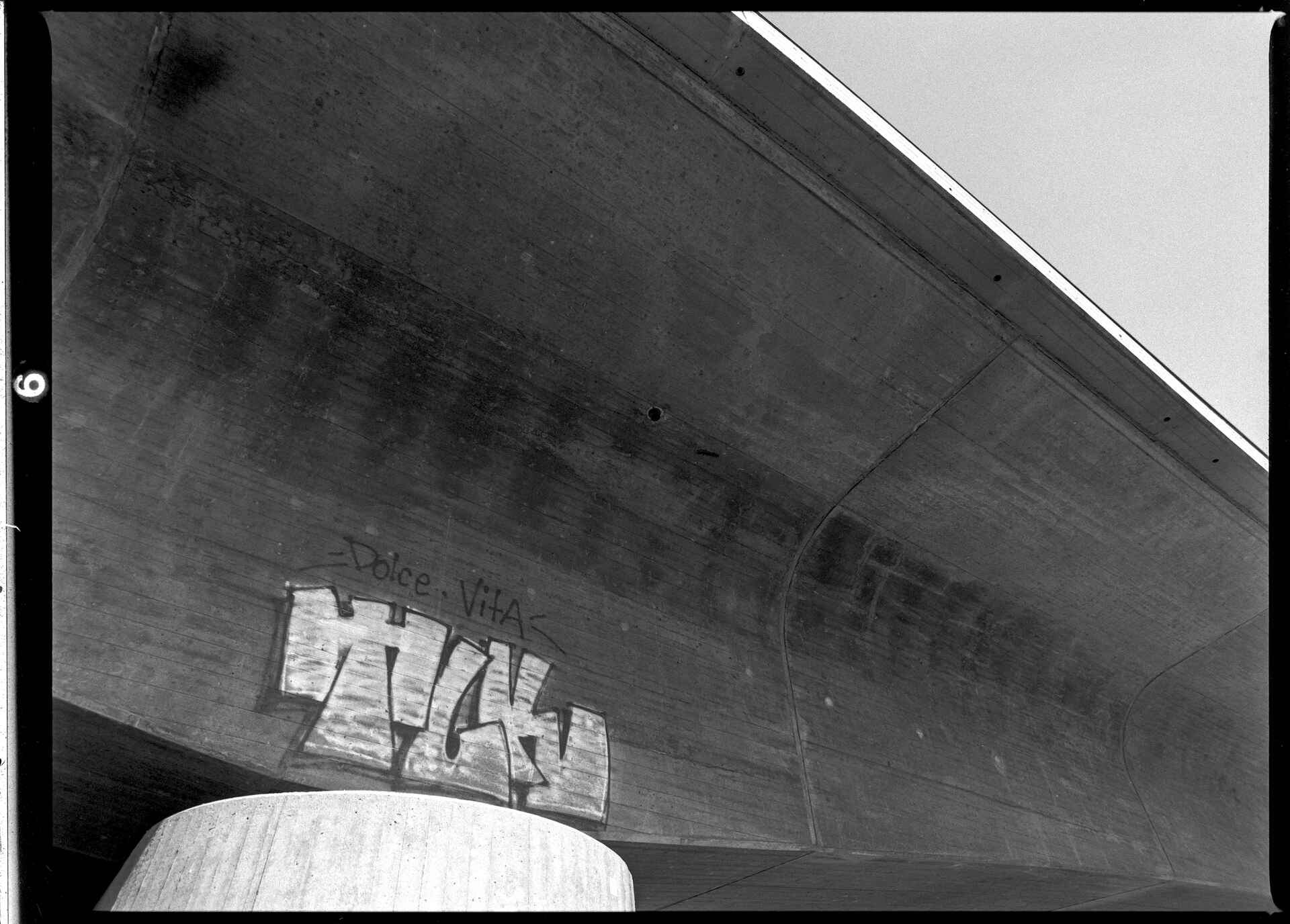 Kirchentellinsfurt, Tübingen Schwarzweißbild (digitalisiert vom Fomapan-100-Rollfilmnegativ): Graffiti an einer Betonbrücke bei Kirchentellinsfurt/Tübingen: ›Dolce Vita‹.