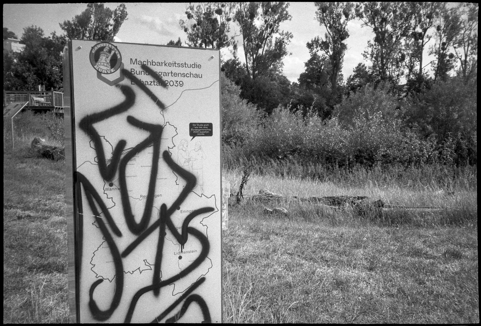 Schwarzweißbild (digitalisiert vom Ilford-Delta-400-Kleinbild-Negativ): Infotafel zur geplanten Bundesgartenschau 2039 im Echaztal.