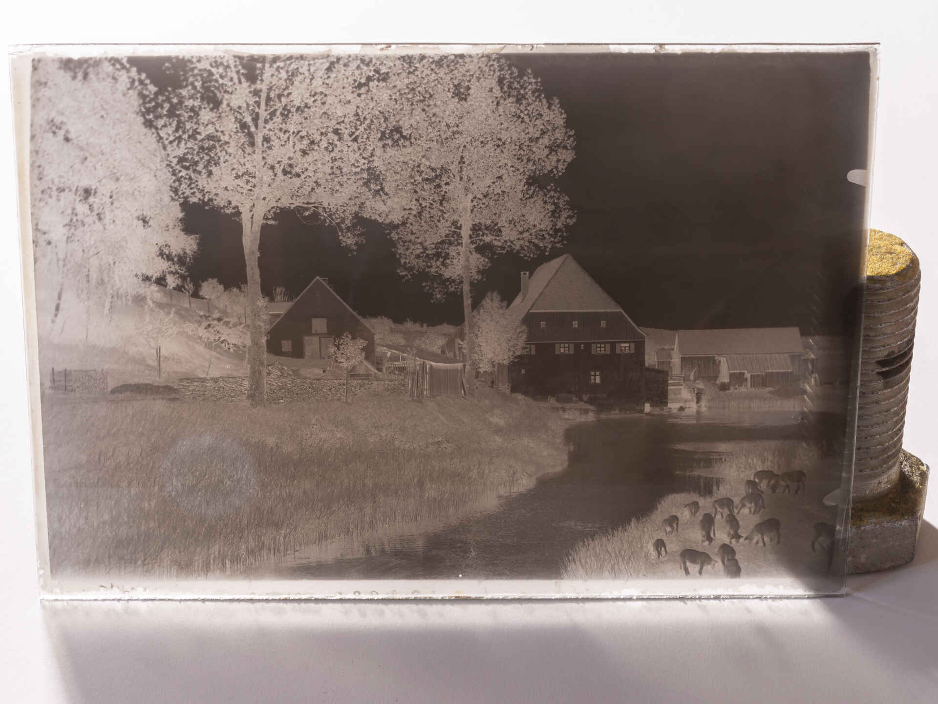 Farbbild (born-digital): Stehendes Glasnegativ, angelehnt an eine große Schraube. Die Platte zeigt die Schrezheimer Mühle bei Ellwangen, ca. 1905. (Foto: Martin Frech, 2/2026)