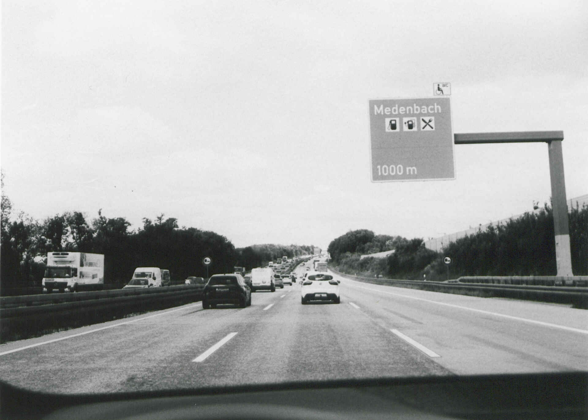 Unterwegs auf der A3 (Foma Ortho 400/Fomabrom Variant 111) (Foto: Martin Frech, 5/2025) Schwarzweißfoto: Das Bild zeigt die Autobahn A3 und ein Schild mit dem Hinweis auf die Raststätte Medenbach; zwischen den Ausfahrten Niedernhausen und Limburg-Süd. (Foto: Martin Frech, 5/2025)