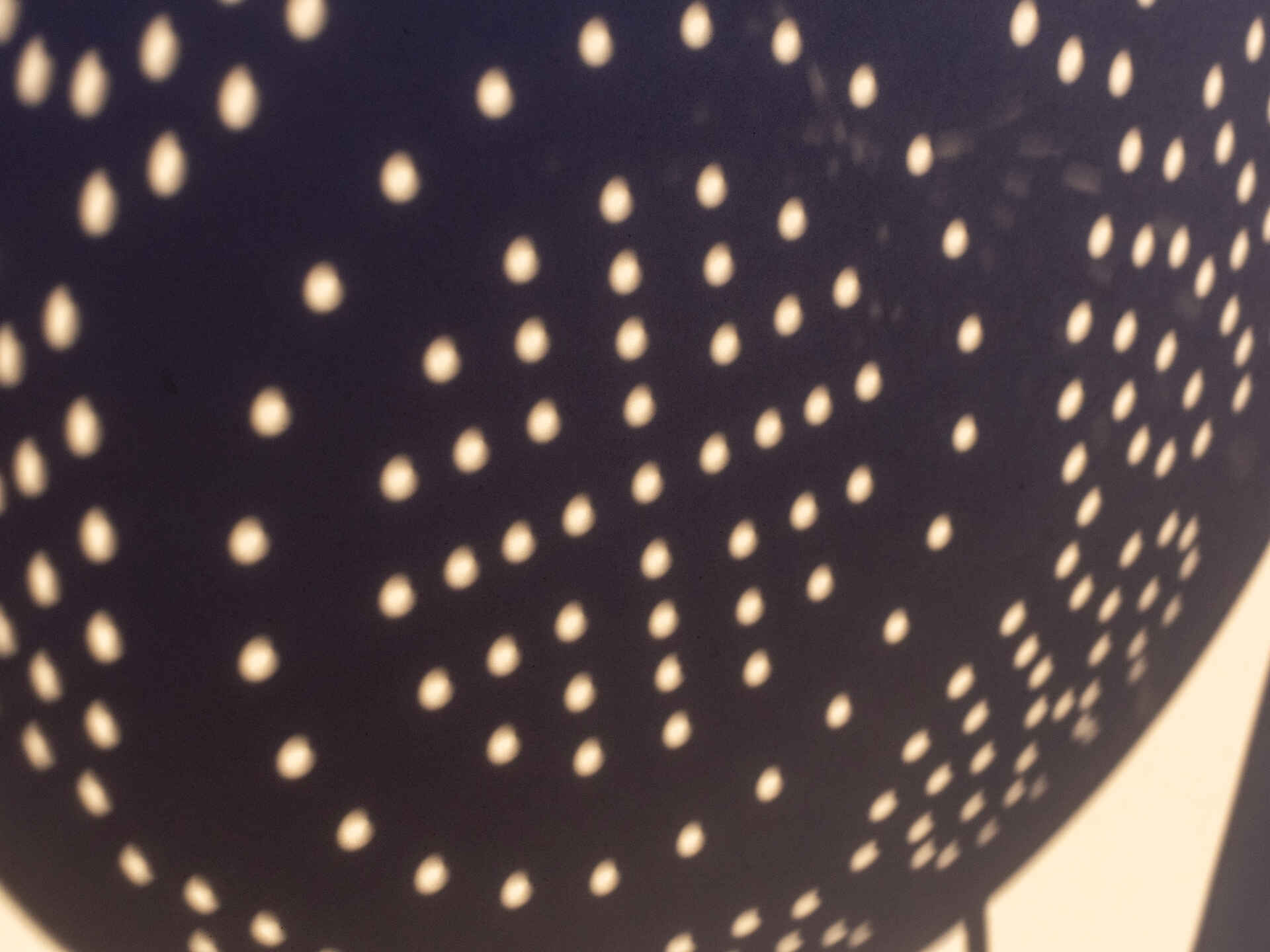 Der Mond schiebt sich dazwischen: Die Sonne wirkt wie angeknabbert. Farbbild (born digital): Das Bild der teilweise bedeckten Sonne wird durch ein Nudelsieb auf einen weißen Karton projiziert.