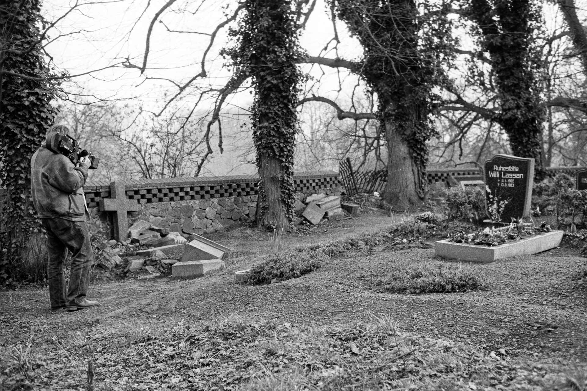 Peter Krieg (Foto: Martin Frech, 2/1990) Schwarzweißbild: Peter Krieg filmt mit seiner 16mm-Aaton-Kamera auf einem Friedhof. (Foto: Martin Frech, 2/1990)