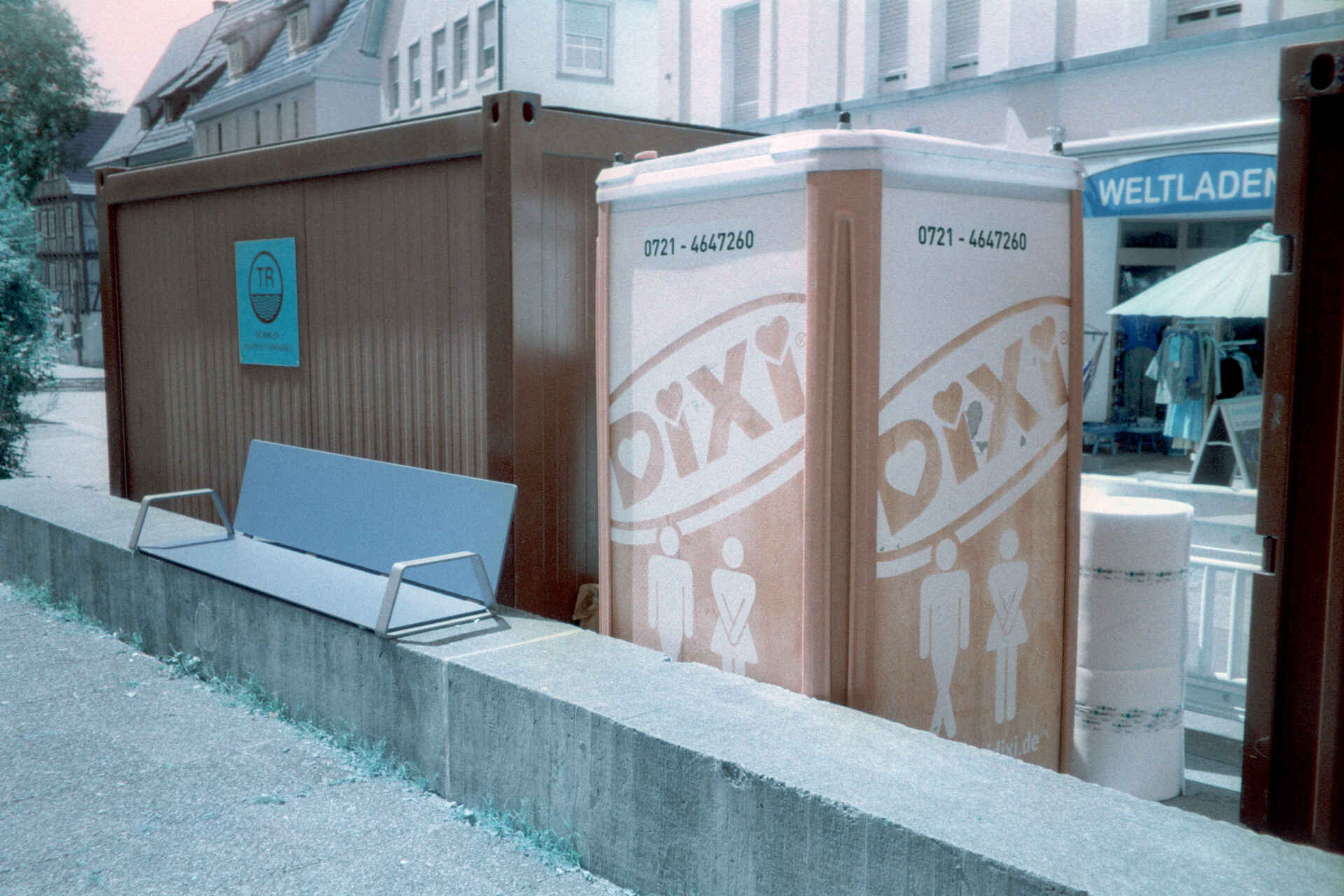 Farbbild (invertiertes Digitalisat des Falschfarben-Colornegativs): Dixi-Klo neben einem Baucontainer in Reutlingen. (Foto: Martin Frech, 7/2026)