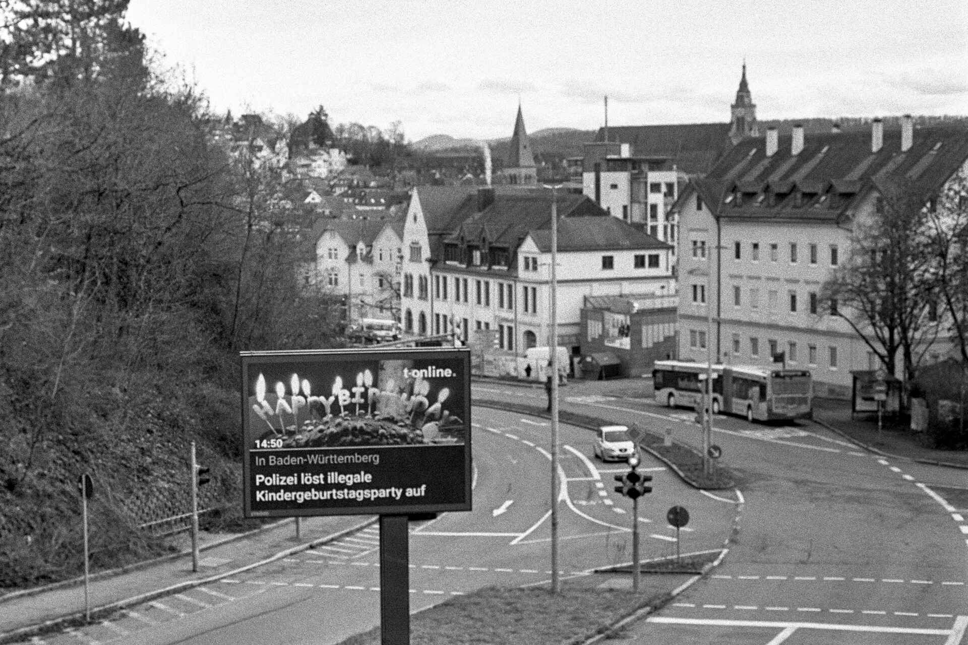 Schwarzweißbild (Scan vom Ilford-HP5+-Negativ): Nachricht über die Auflösung einer Kindergeburtstagsfeier auf einer selbstleuchtenden Werbetafel in Tübingen. (Foto: Martin Frech, 2/2021)