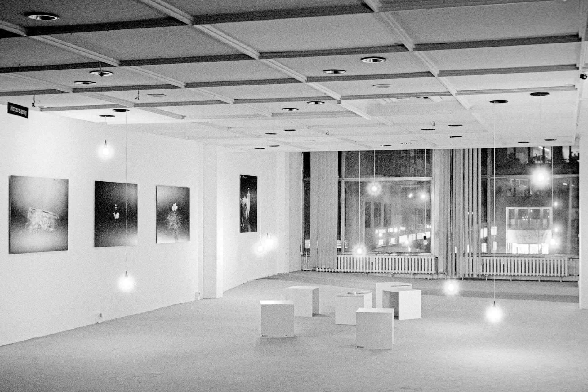 Großer Raum mit abgehängter Decke, raumhohe Fenster, auf dem Boden Sitzwürfel, an der Wand hängen auf Platten kaschierte Fotografien (provisorische Zwischennutzung). (Foto: Martin Frech, 11/2007)