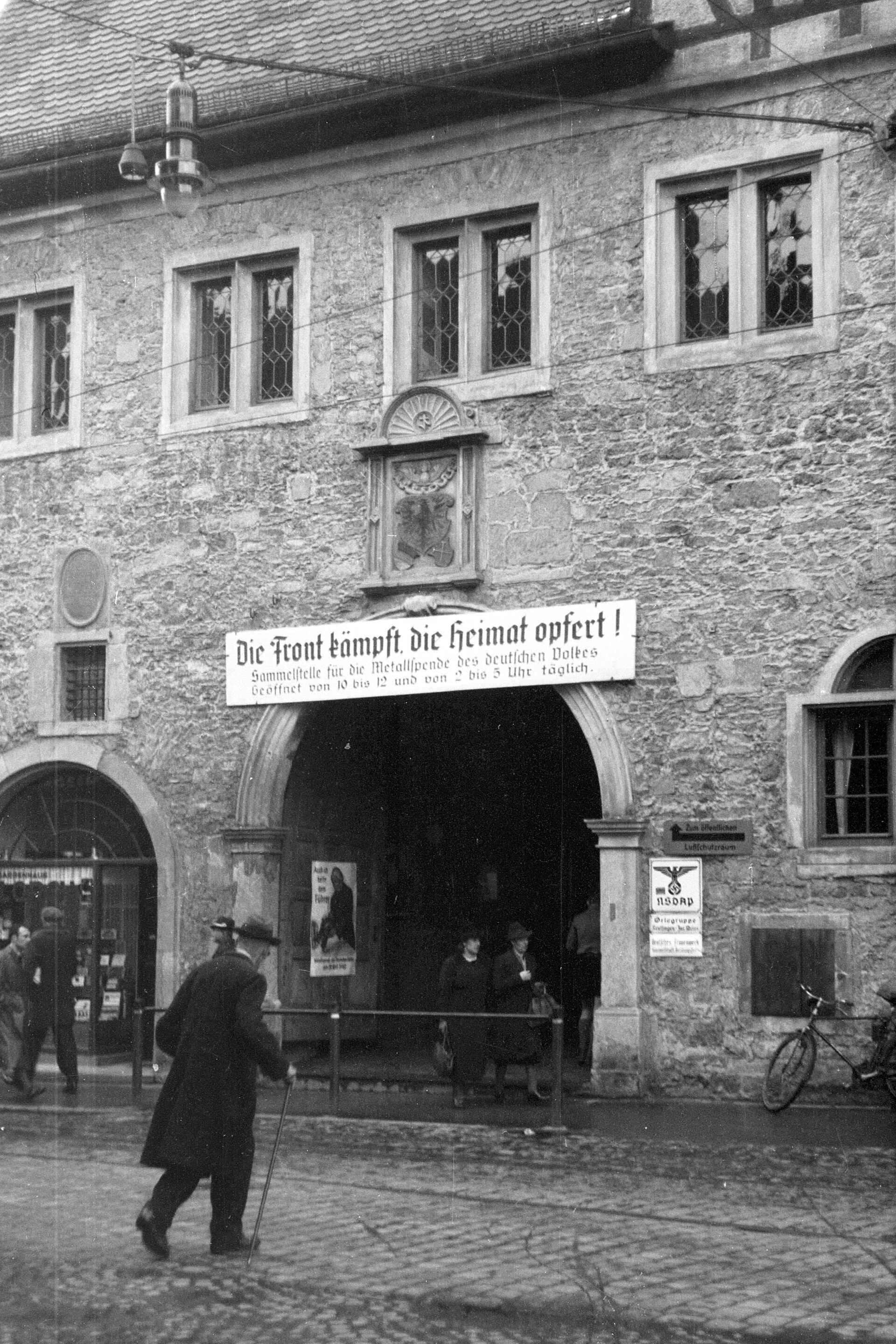 Spitalhof an der Wilhelmstraße in Reutlingen, 1940er-Jahre (Foto: StadtA Rt./Näher, 1940) Schwarzweißbild (Scan vom Kleinbildnegativ): Fassade und Eingang des Spitalhof an der Wilhelmstraße in Reutlingen. Über dem Torbogen ist ein Schild angebracht: ›Die Front kämpft, die Heimat opfert! Sammelstelle für die Metallspende des deutschen Volkes‹
