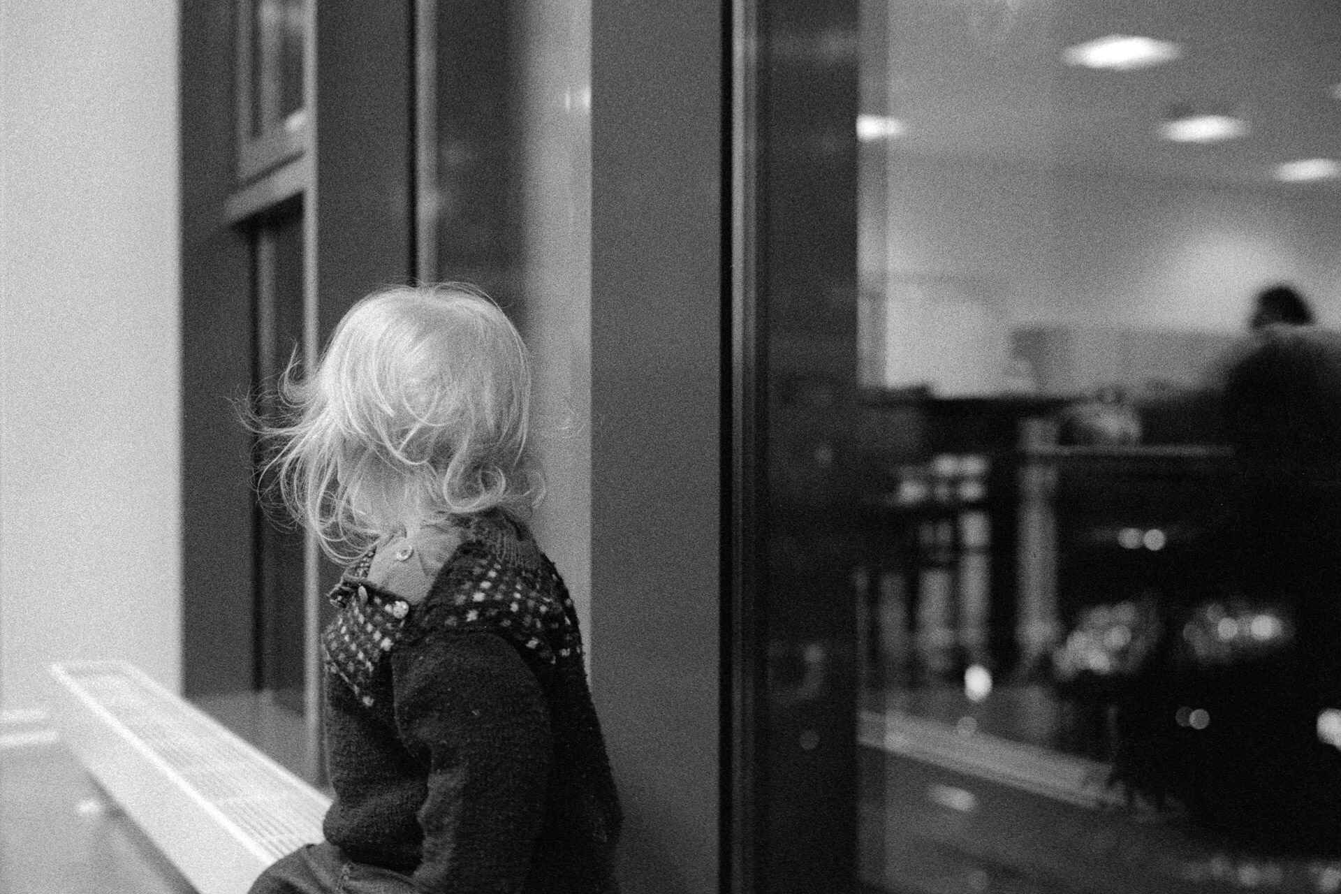Stadtbücherei, Berlin (Foto: Martin Frech, 2/2008) Schwarzweißbild: Ein Kind sitzt auf einem Heizkörper am Fenster, den Kopf abgewandt. (Foto: Martin Frech, 2/2008)