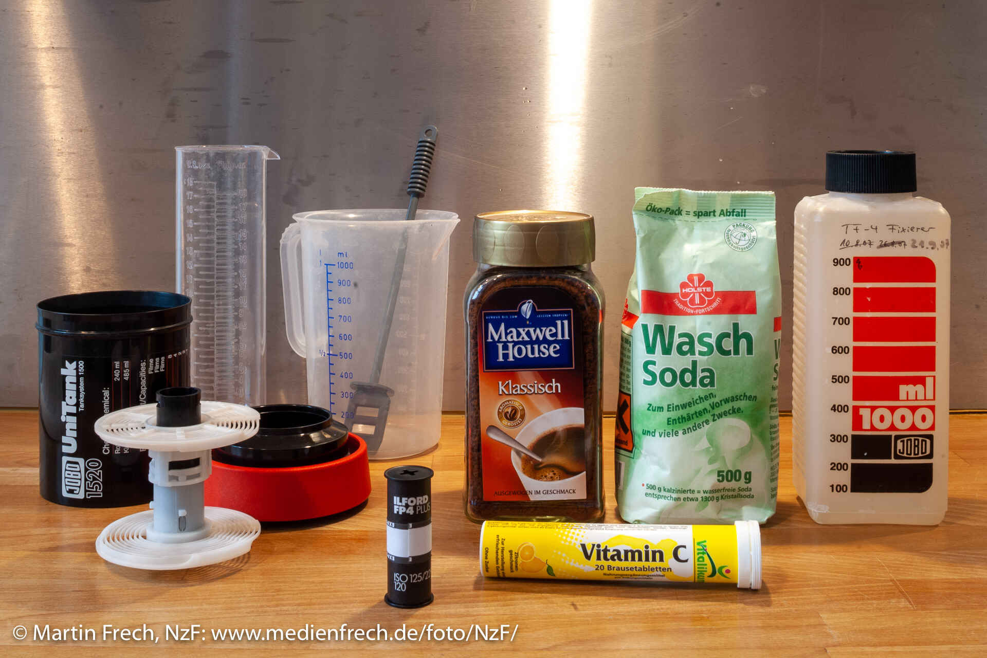 Stilleben mit Entwicklungsdose, Meßbecher, Mensur, einem Glas mit Instant-Kaffeepulver, einem Beutel Waschsoda und einer Rolle Vitamin-C-Tabeletten sowie einem belichteten Rollfilm (Farbbild) (Foto: Martin Frech, 9/2007)