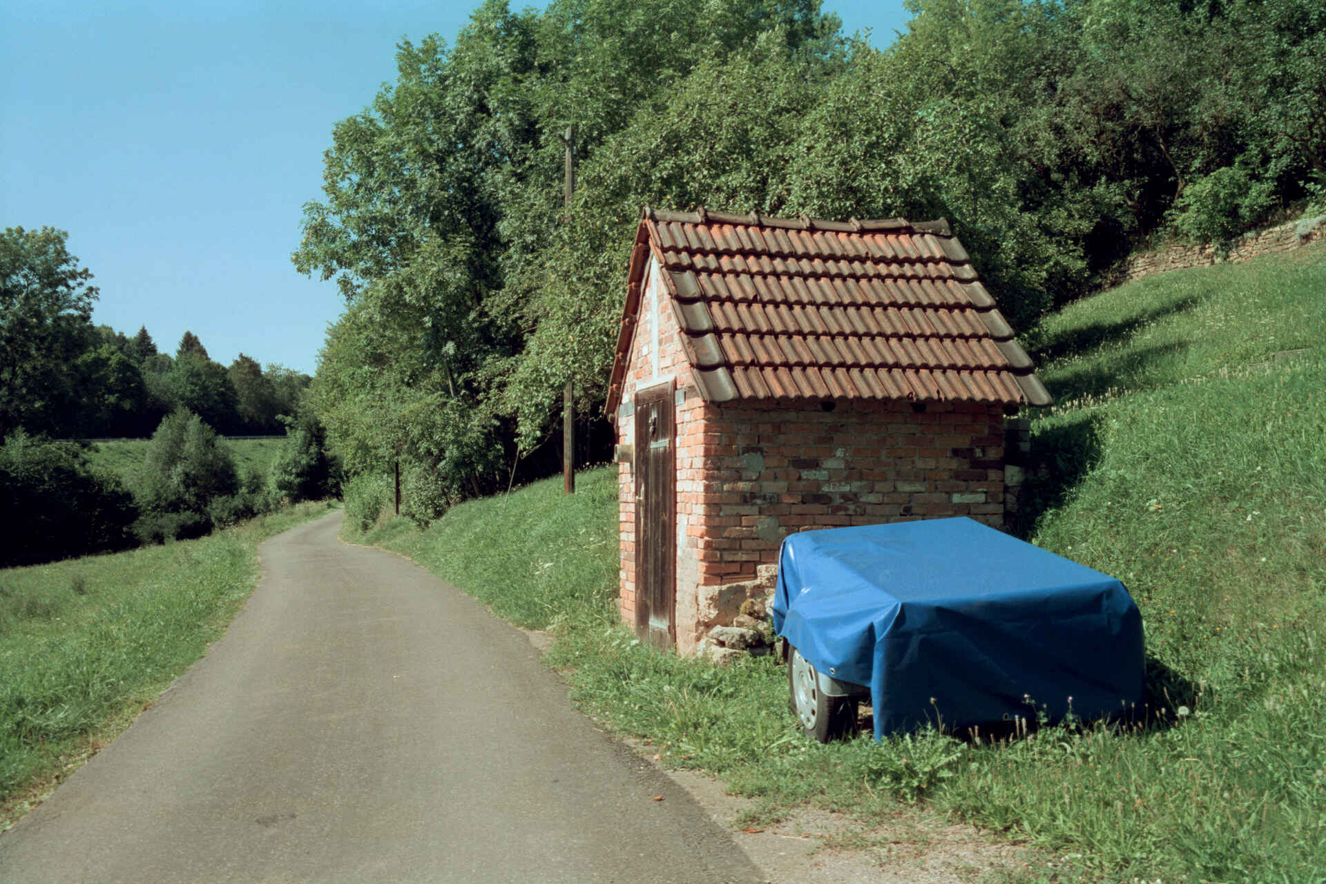 Farbbild: Brunnenhäuschen neben einem Feldweg im Grünen. (Foto: Martin Frech, 8/2017)