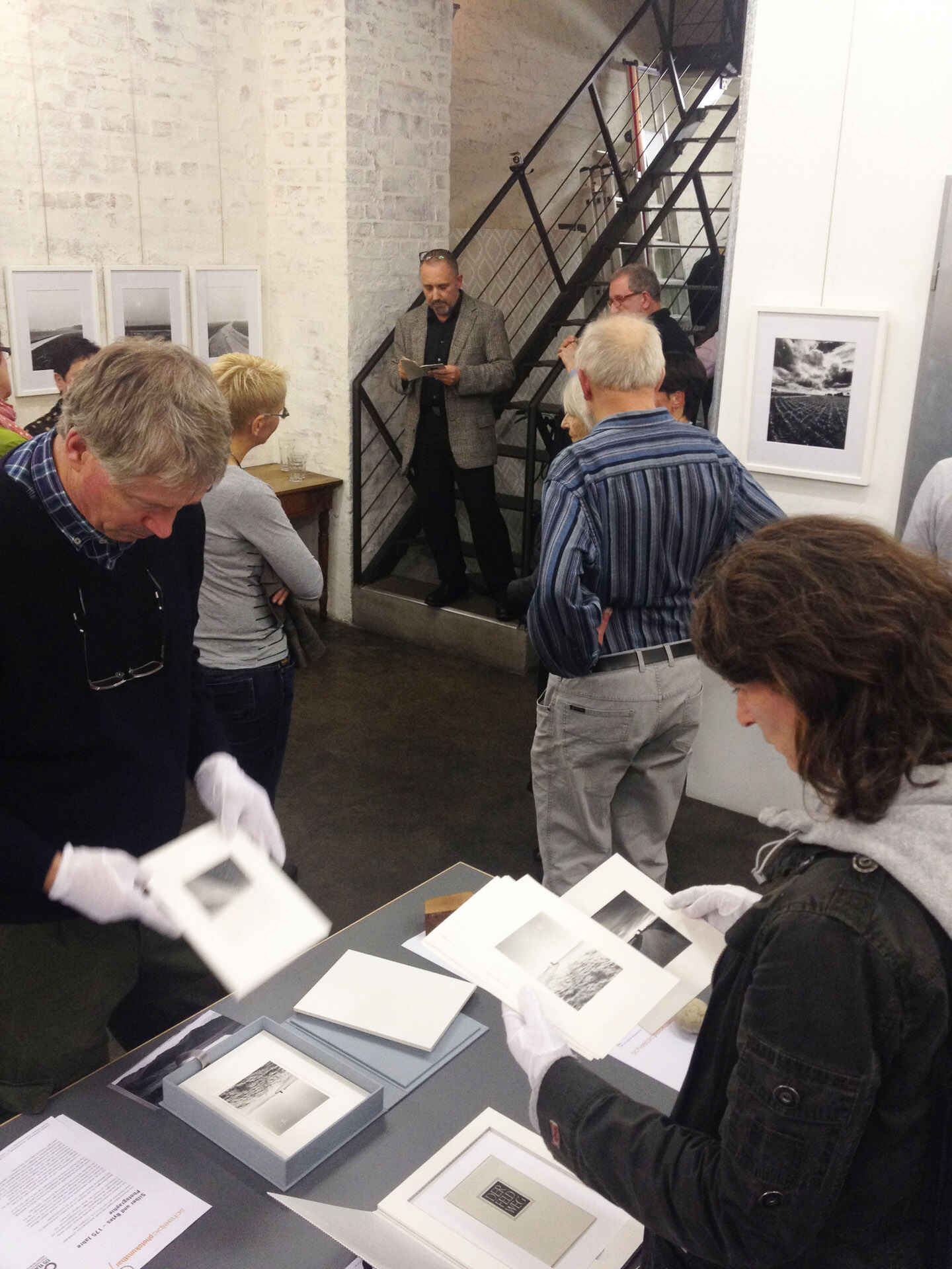 Farbbild: Tobias D. Kern liest aus einem Text vor in der schaelpic photokunstbar, Köln. Im Vordergrund schauen Besucherinnen und Besucher Fotos an. (Foto: Annette Völckner, 10/2013)