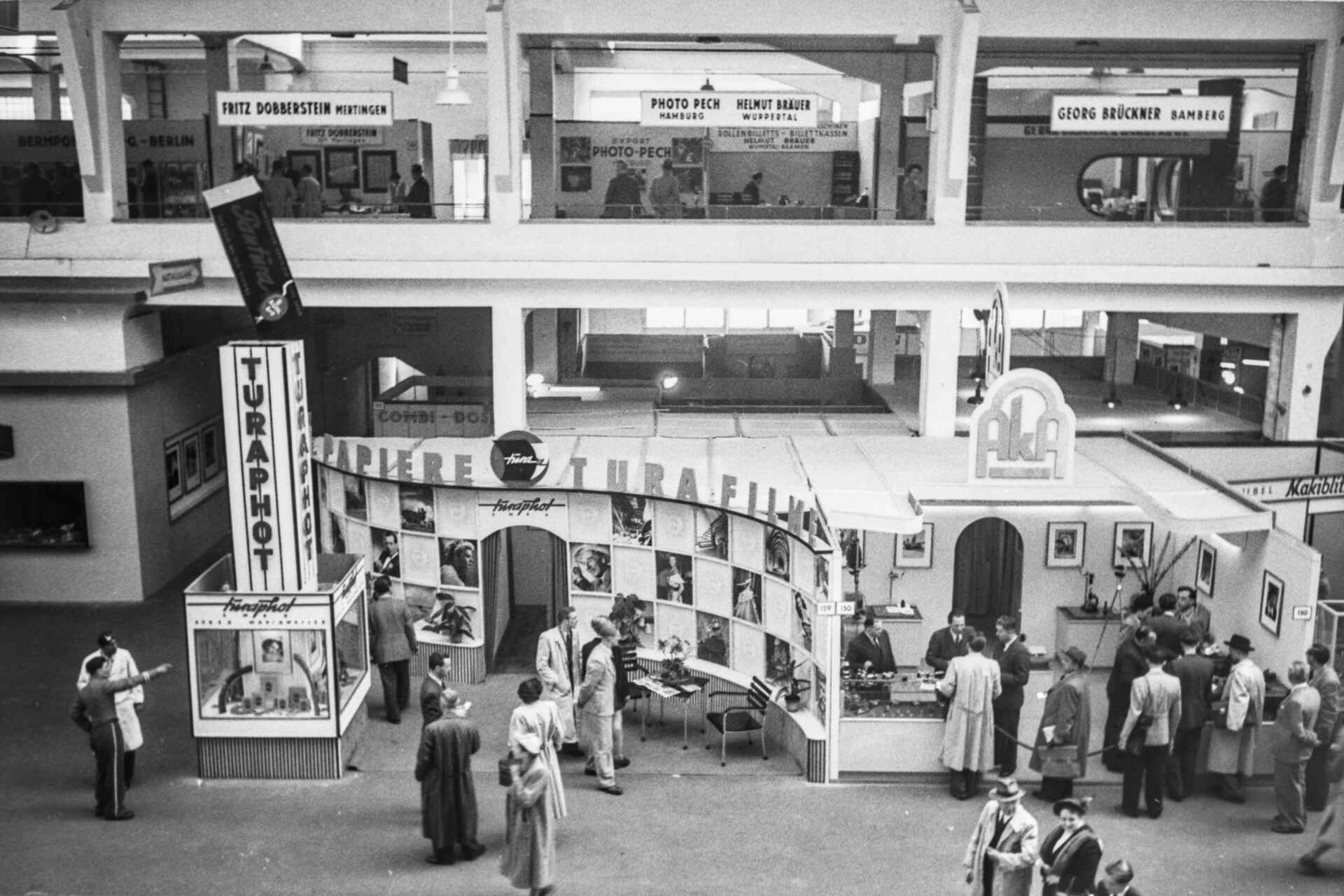 Schwarzweißbild (Scan vom Negativ): Blick in eine Messehalle der ersten photokina 1951 auf die Stände von Turaphot und Aka.